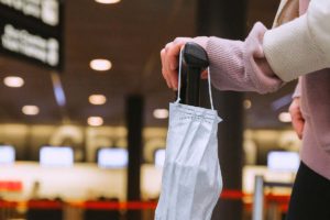 Woman holding a mask and luggage at an airport
