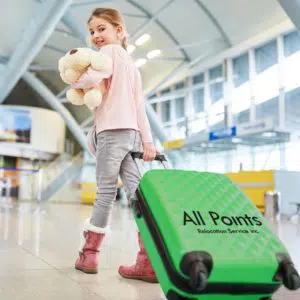 Girl with a green luggage and a teddy bear in an airport.