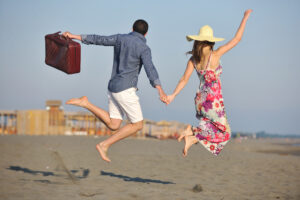 Couple on beach with travel bag representing freedom and fun honeymoon concept