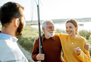 Young man and woman with senior grandfather dressed in sweaters spending a good time together while fishing in the morning