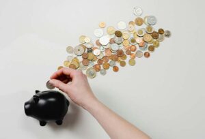 A black piggy bank with a hand adding a coin and various coins spread out across a table